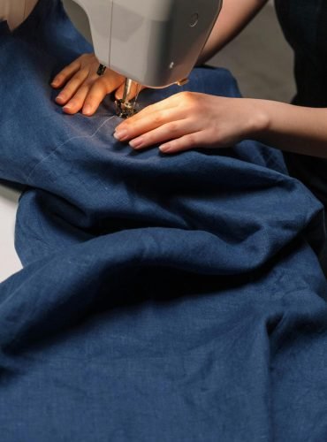 Hands working on a sewing machine stitching blue denim fabric.